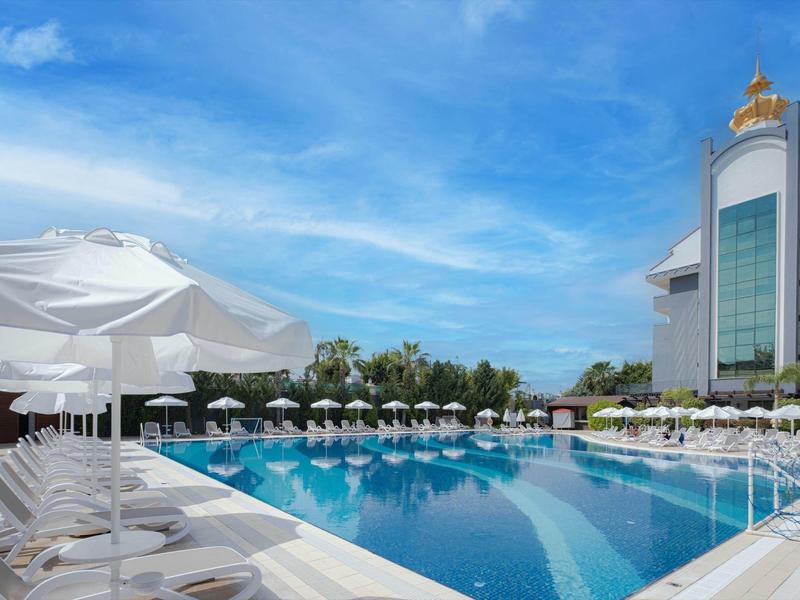 Outdoor hotel pool area with white umbrellas, lounge chairs, and a modern building.