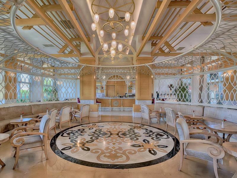 Luxury hotel lobby with circular seating, intricate ceiling, and marble floor with ornate design.