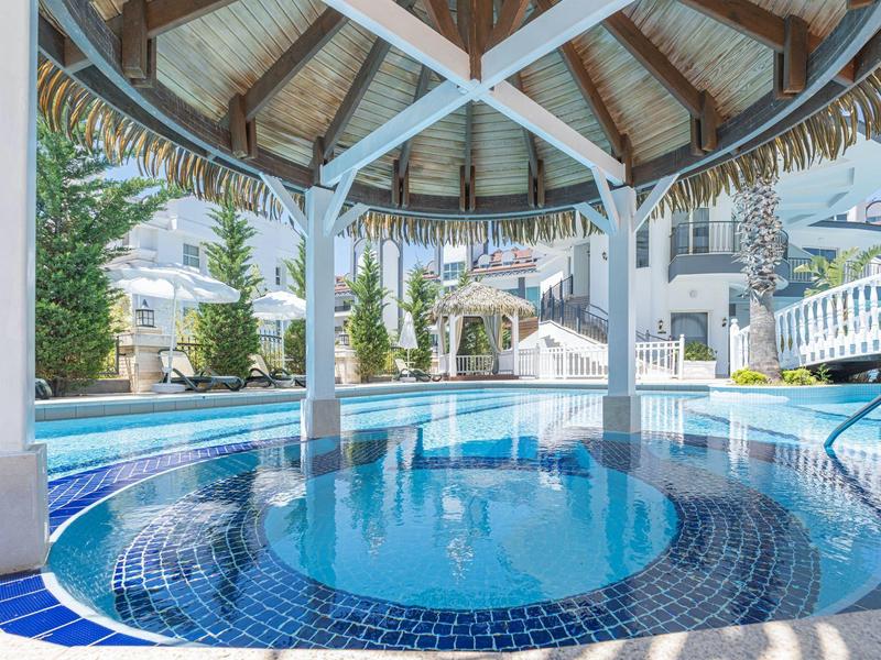 Sunny outdoor pool area with circular swim-up bar under thatched roof.