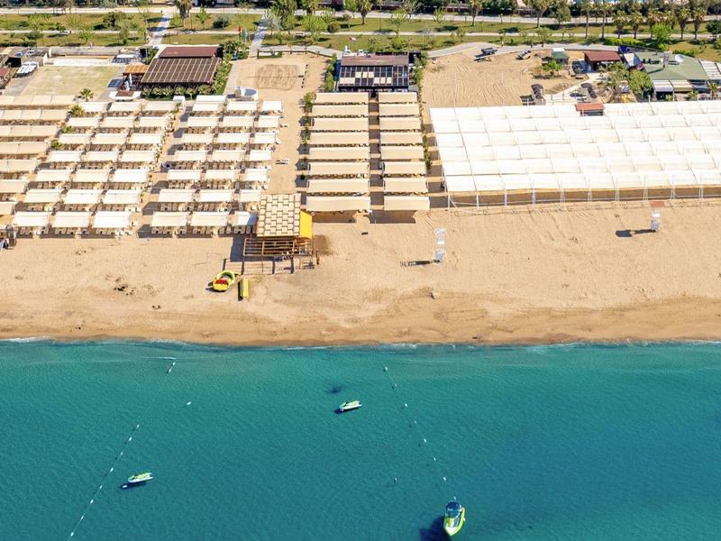 Aerial view of a beach with sunbeds, umbrellas, a wooden pier, and turquoise sea water.
