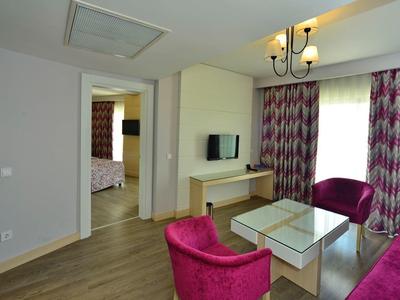 Moderní obývací pokoj s růžovým nábytkem, velkým oknem a dřevěnou podlahou.