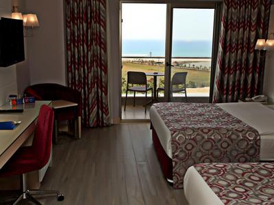 Hotelový pokoj se dvěma postelemi, výhled na terasu a moře přes velké posuvné skleněné dveře.