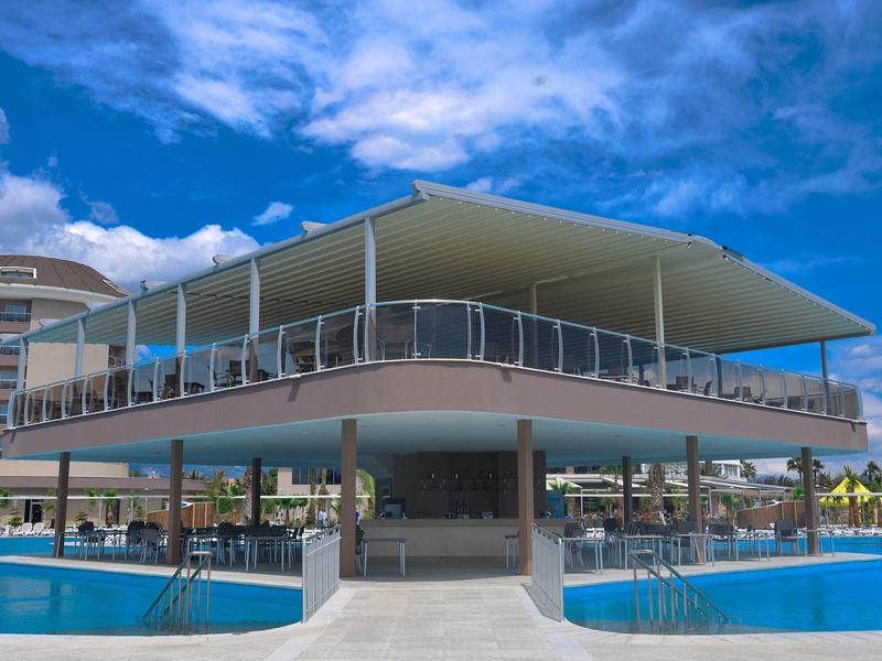 Moderní dvoupatrová budova u bazénu s terasou a modrou oblohou.