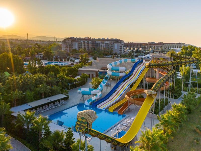 Vodní park s barevnými skluzavkami a bazény při západu slunce v hotelovém areálu.
