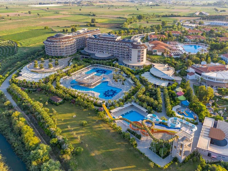 Velký resort s několika bazény obklopený zelení a zemědělskými poli.