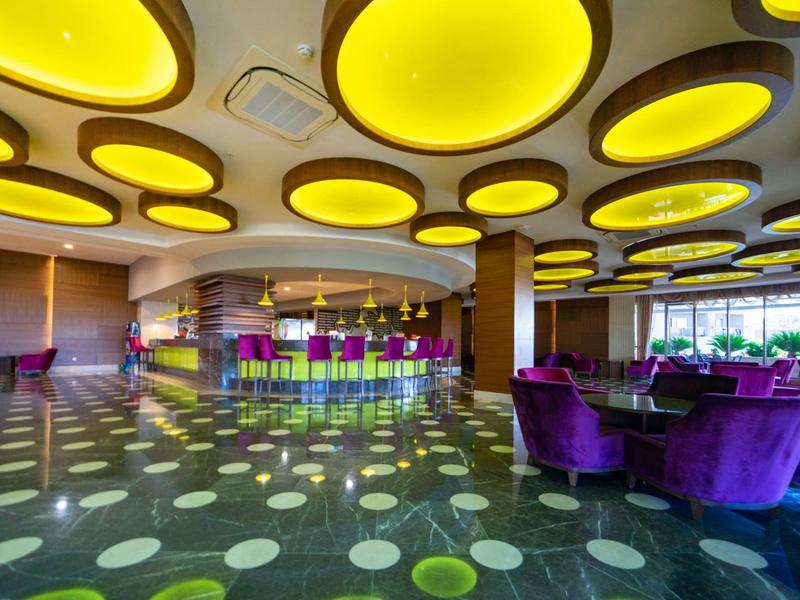 Moderní hotelová lobby s barevnými barovými židlemi, fialovými křesly a žlutými stropními světly.