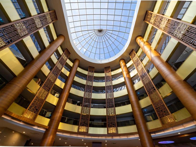 Pohled vzhůru na kruhové hotelové lobby s vysokými sloupy a skleněnou kupolí.