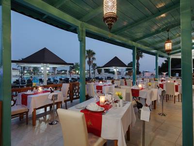 Buitenrestaurant met witte tafels, rode accenten en avondverlichting bij een zwembad.