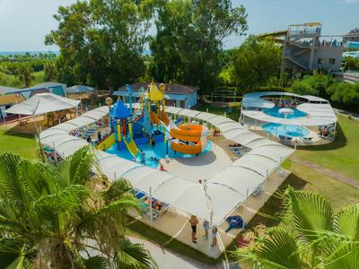 Kleurrijke waterspeeltuin met glijbanen en zonbescherming in een groene hotelomgeving.