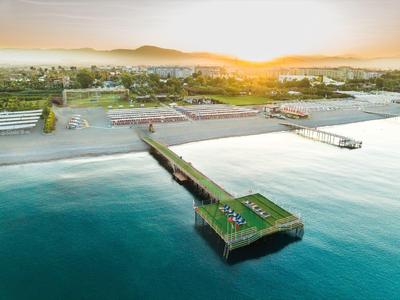 Zonsondergang aan een kuststrand met een lange pier in kalm water en zonaanbidders op het strand.