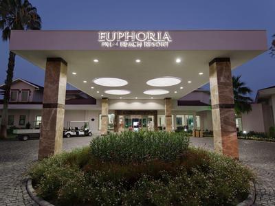 Twee mensen spelen tennis op een buiten rode kleibanen omgeven door palmbomen en groen.