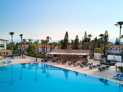 Groot hotelzwembad met ligstoelen en palmbomen onder een heldere lucht