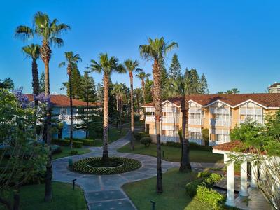 Hotelcomplex met meerdere gebouwen, palmbomen en een geplaveid pad onder een heldere blauwe lucht.