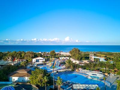 Uitzicht op een resort met zwembaden en groen bij de zee onder een blauwe lucht.