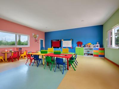 Kleurrijke speelkamer met kleine tafels en stoelen tegen kleurrijke muren en ramen.