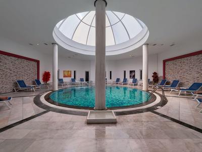 Rond overdekt zwembad met glazen koepel en ligstoelen binnen.