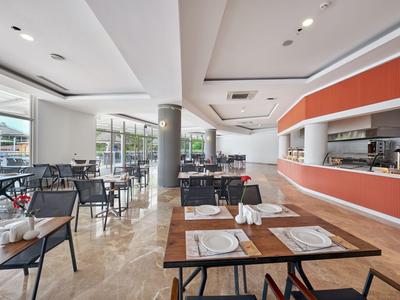 Modern restaurant met grote ramen, zwarte stoelen en een oranje balie.