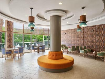 Moderne hotellobby met ronde zitplek en grote ramen met uitzicht op groen.