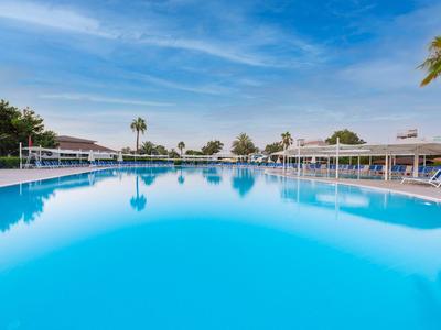 Großer blauer Swimmingpool mit Liegestühlen und Palmen unter blauem Himmel.