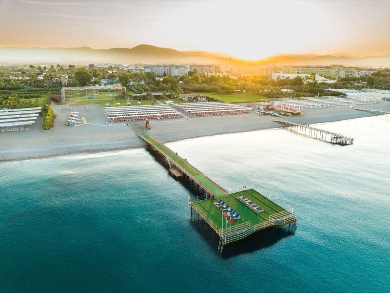 Zonsondergang aan een kuststrand met een lange pier in kalm water en zonaanbidders op het strand.
