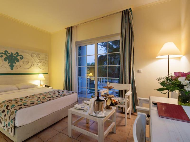 Gezellige hotelkamer met tweepersoonsbed, lampen, flatscreen-tv, bloemen en raam met gordijnen.