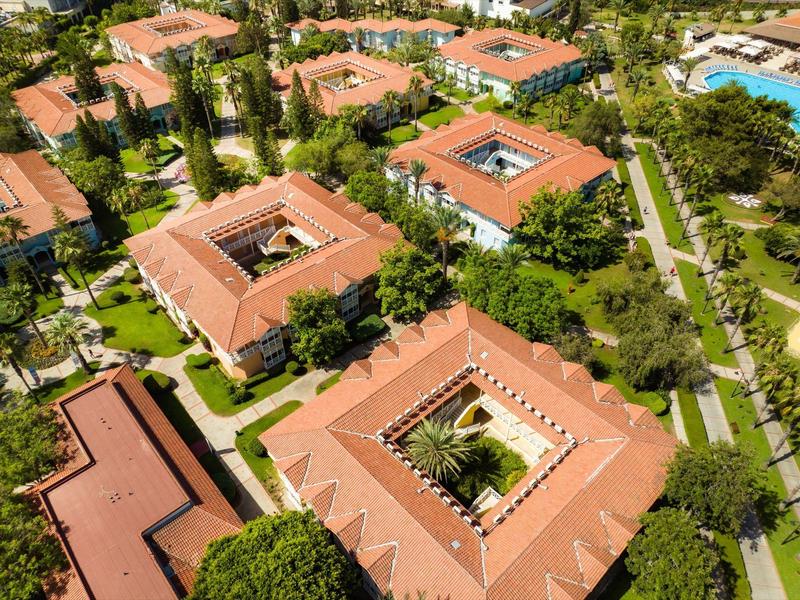 Luchtfoto van binnenplaatsgebouwen met terracotta daken omringd door groene gazons en bomen.