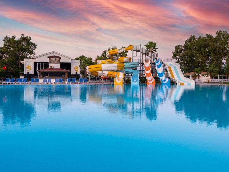 Groot buitenzwembad met glijbanen en kleurrijke zonsondergang bij een resort.