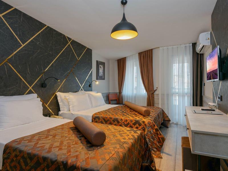 Hotelkamer met twee eenpersoonsbedden, bruin beddengoed, zwarte muur en groot raam met gordijnen.