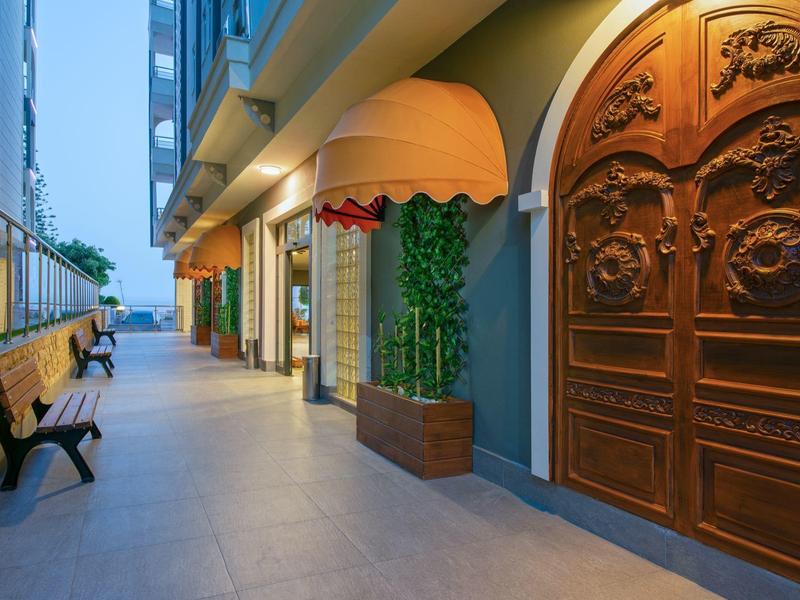 Helder verlichte hotelgang met gesneden houten deur en banken langs de muur.