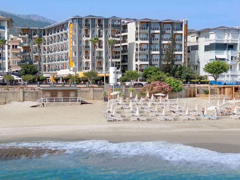 Modern hotel aan het zandstrand met ligstoelen en kalme blauwe zee onder een heldere hemel.