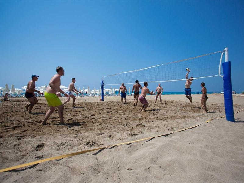 Jeunes jouant au volley-ball sur une plage ensoleillée avec ciel bleu clair.