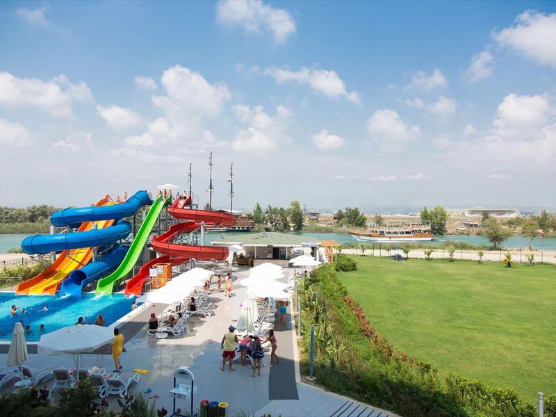 Toboggans colorés et pelouse verte sous un ciel bleu clair dans un parc aquatique.