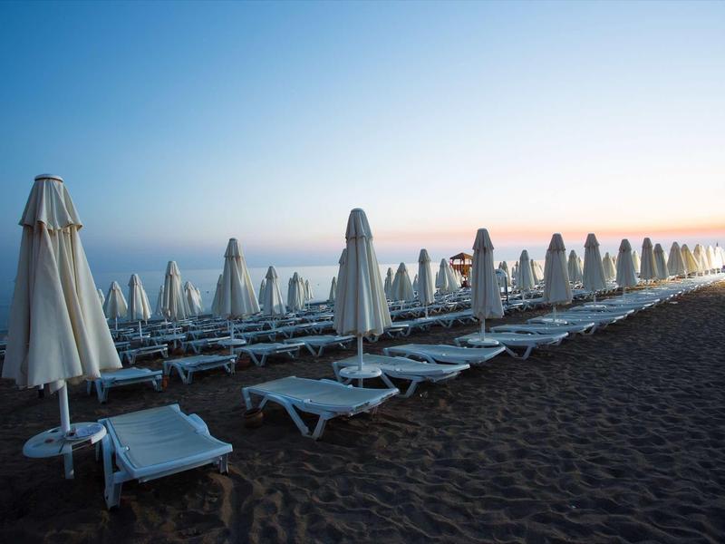 Plage au crépuscule avec chaises longues blanches et parasols fermés alignés sur le sable.