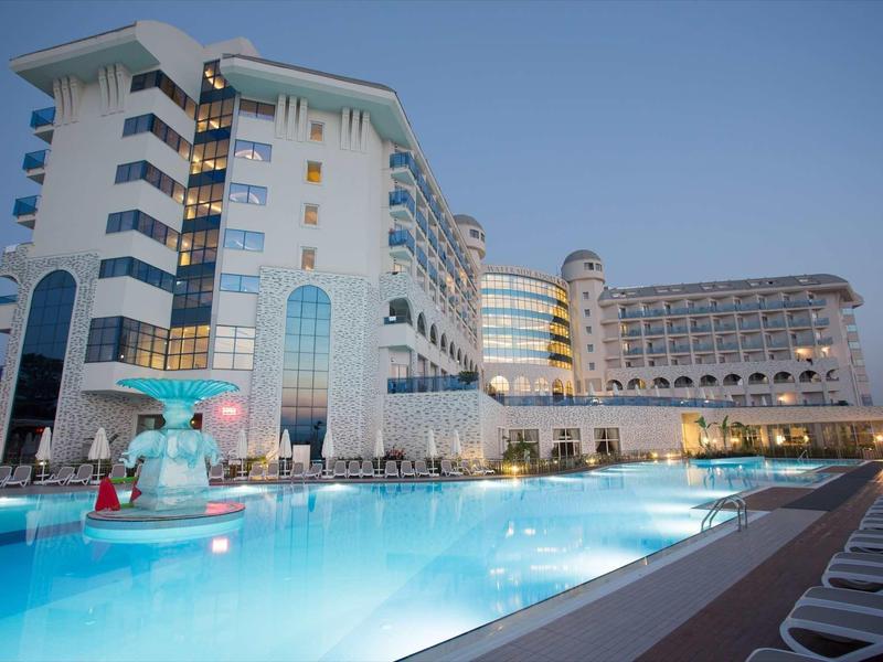 Hôtel moderne avec grande piscine éclairée au crépuscule et chaises longues autour.