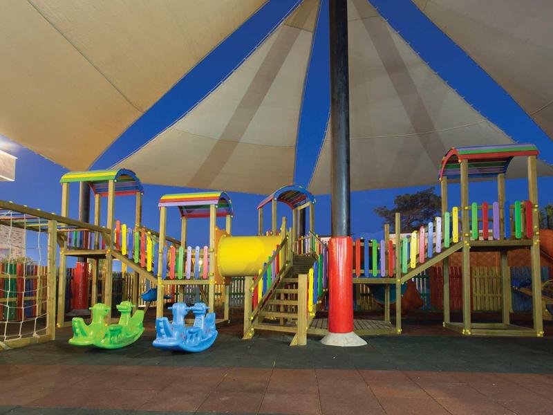 Aire de jeux colorée sous un grand auvent dans une aire de loisirs extérieure.