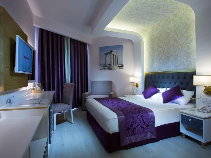 Chambre d'hôtel moderne avec lit double, éclairage doux et décoration violet et blanc.