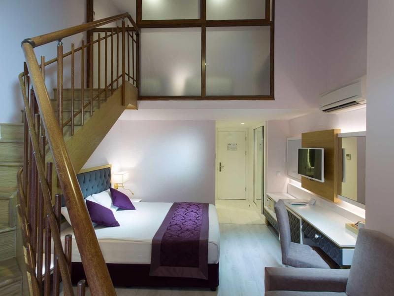 Chambre d'hôtel moderne avec lit double, escalier en bois et mobilier contemporain.