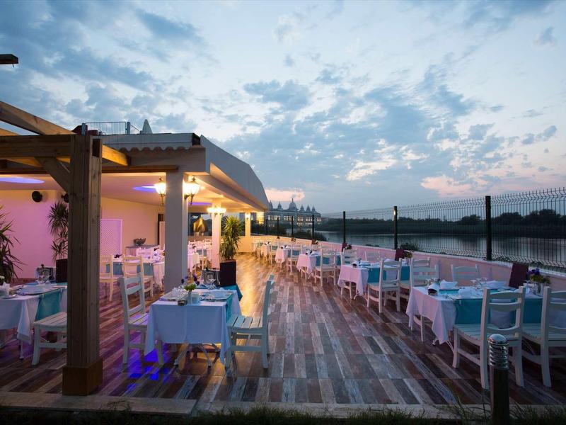 Terrasse de restaurant élégante avec tables blanches au coucher du soleil près d'un lac.