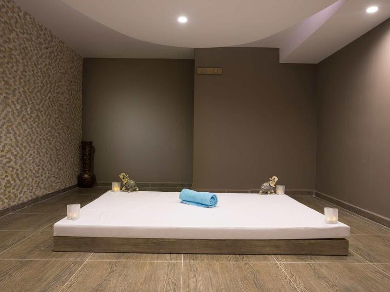 Salle de massage calme avec tapis blanc, serviette bleue et murs brun clair.