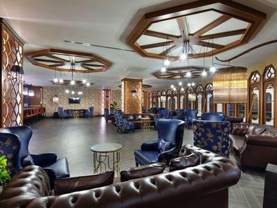 Spacious hotel lounge with brown leather sofas, blue armchairs, and decorative ceiling lights.