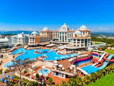 Luxury resort with large pool area, water slides, and sun loungers under clear blue sky.