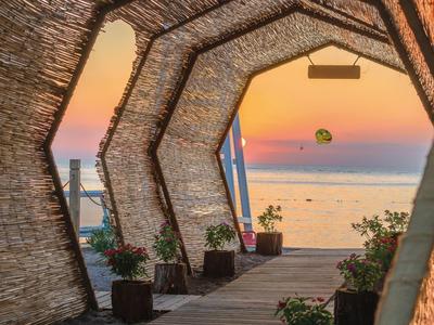 Pohled přes dřevěnou krytou strukturu na západ slunce nad mořem s parasailingem.