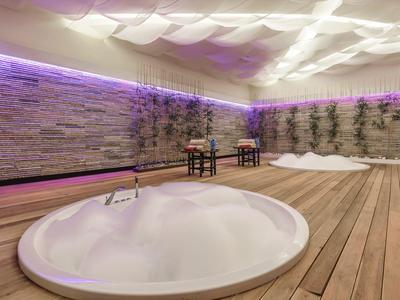 Round whirlpool in a room with wooden floor and illuminated stone wall.
