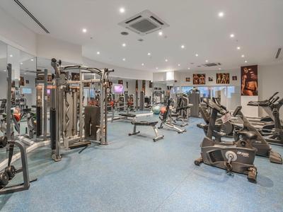 Bright gym with various exercise equipment on blue carpet flooring.