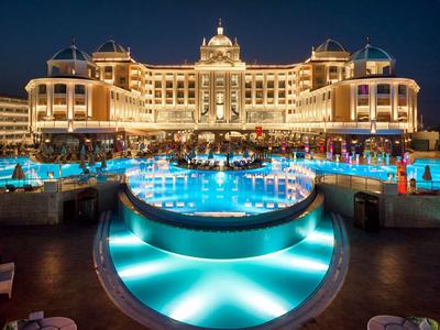 Illuminated luxury hotel with large pool and guests at night
