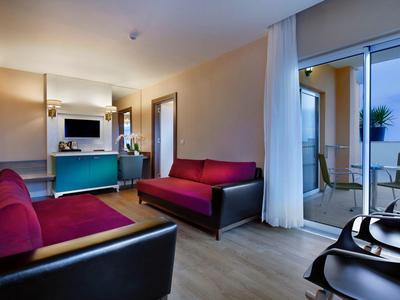 Modern hotel room lounge with red sofas, TV, and access to balcony with table and chairs.