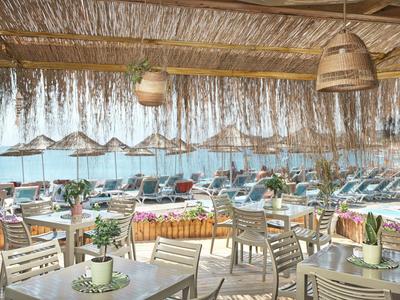 Terrace of a beach restaurant with set tables and view of sun loungers and the sea.