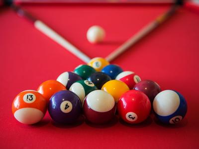 Colorful billiard balls arranged in a triangle on a red table with two cues in the background.