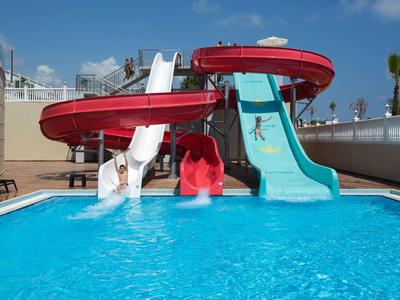 Three water slides lead into a pool under blue sky on a hotel terrace.