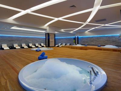 Modern spa area with jacuzzi, sauna, and lounge chairs under indirect lighting.